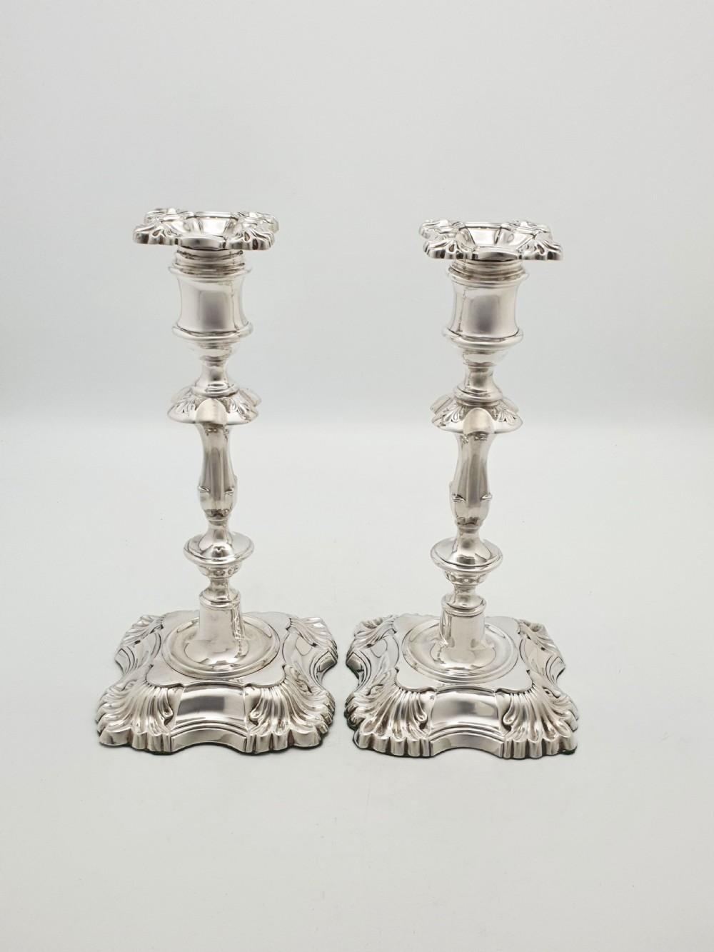 Pair of polished silver-plated Rococo Revival candlesticks with shell motifs and knopped stems on a plain background. View XI