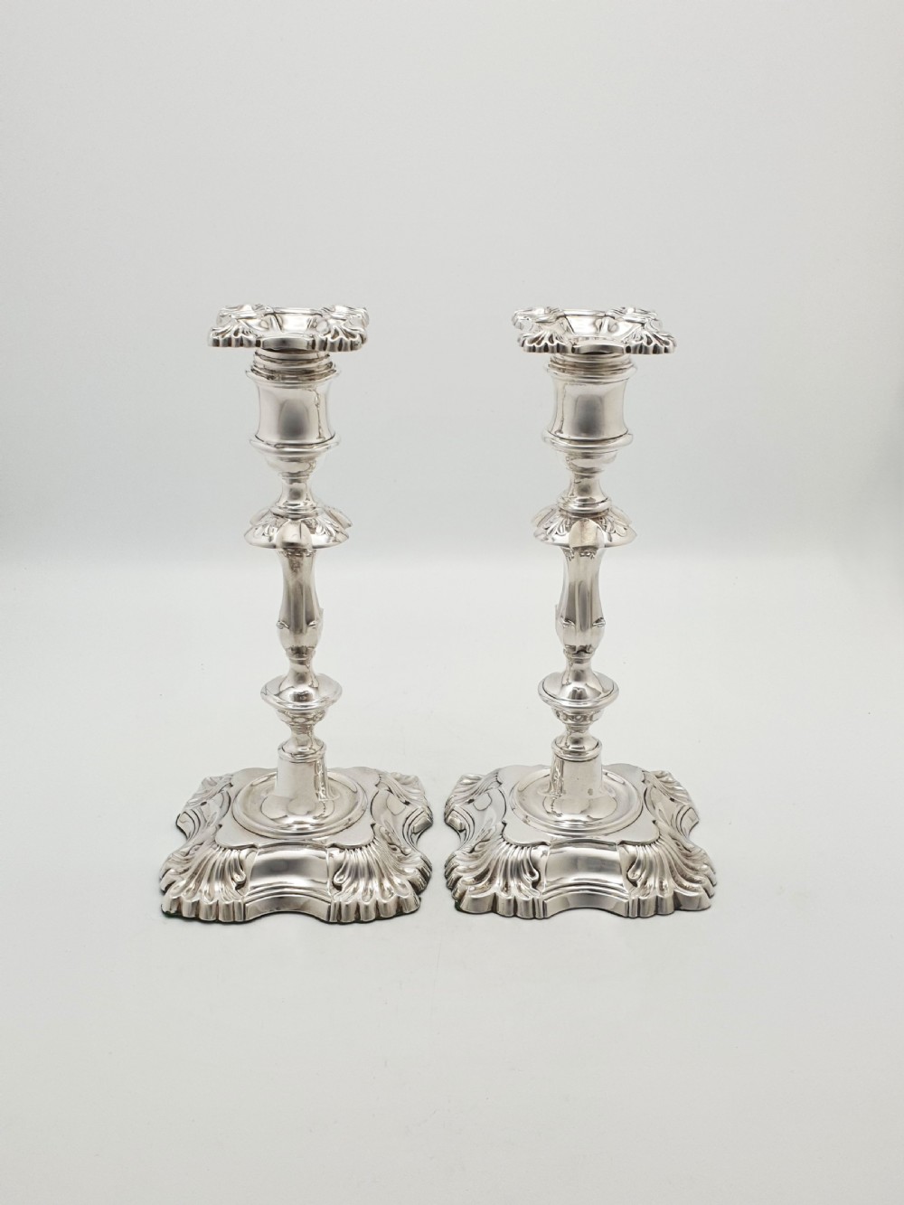 Pair of polished silver-plated Rococo Revival candlesticks with shell motifs and knopped stems on a plain background. View XII