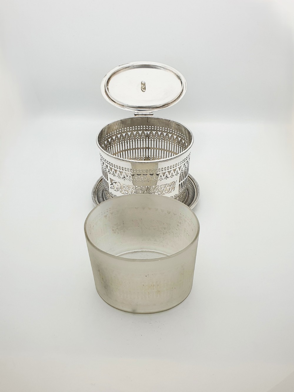 An Edwardian silver plated biscuit barrel featuring pierced scrollwork spelling out the word biscuits, a matching tray base, and a hinged lid with a decorative finial. View IV