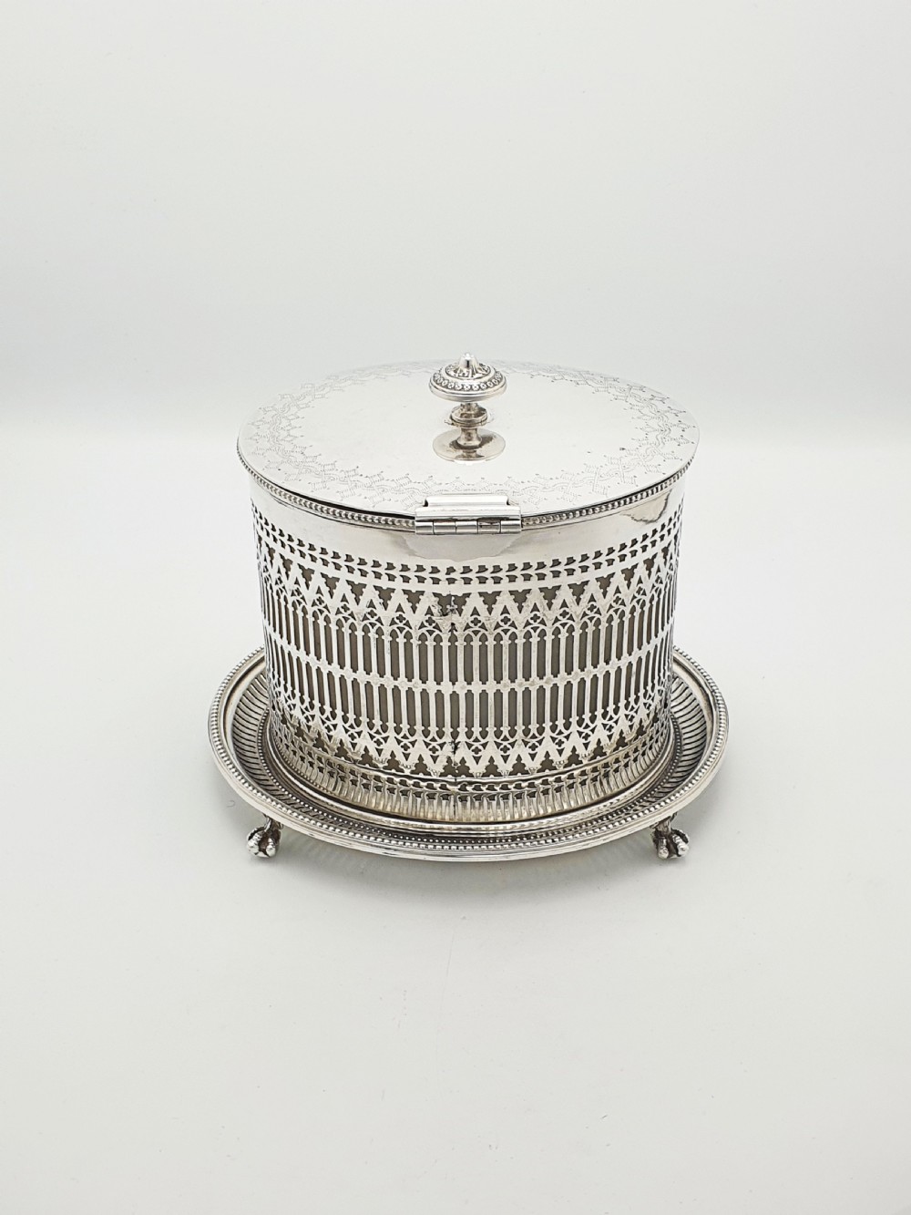 An Edwardian silver plated biscuit barrel featuring pierced scrollwork spelling out the word biscuits, a matching tray base, and a hinged lid with a decorative finial. View VII