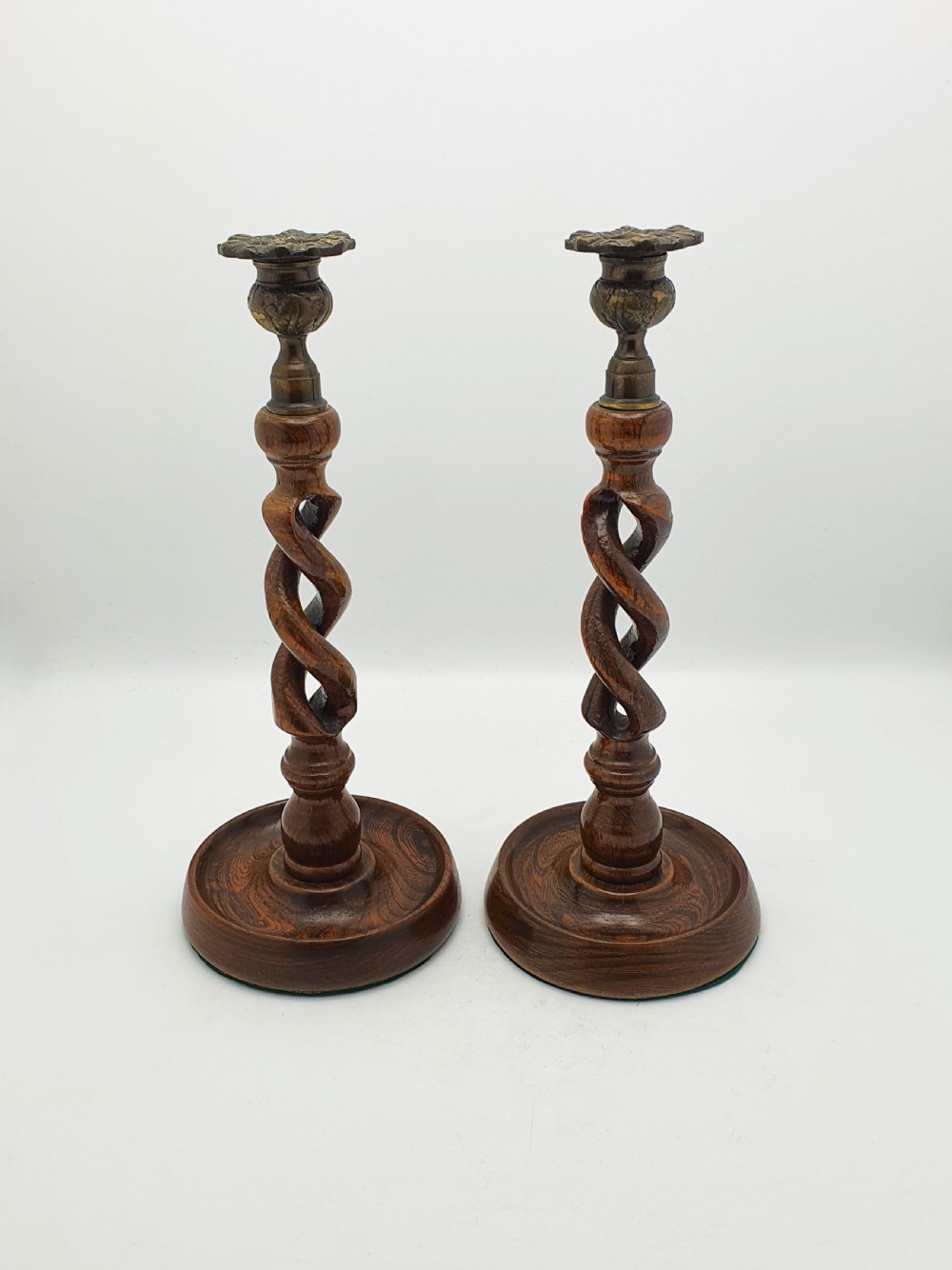 A pair of dark oak candlesticks featuring open barley twist stems and brass sconces atop round dished bases.
