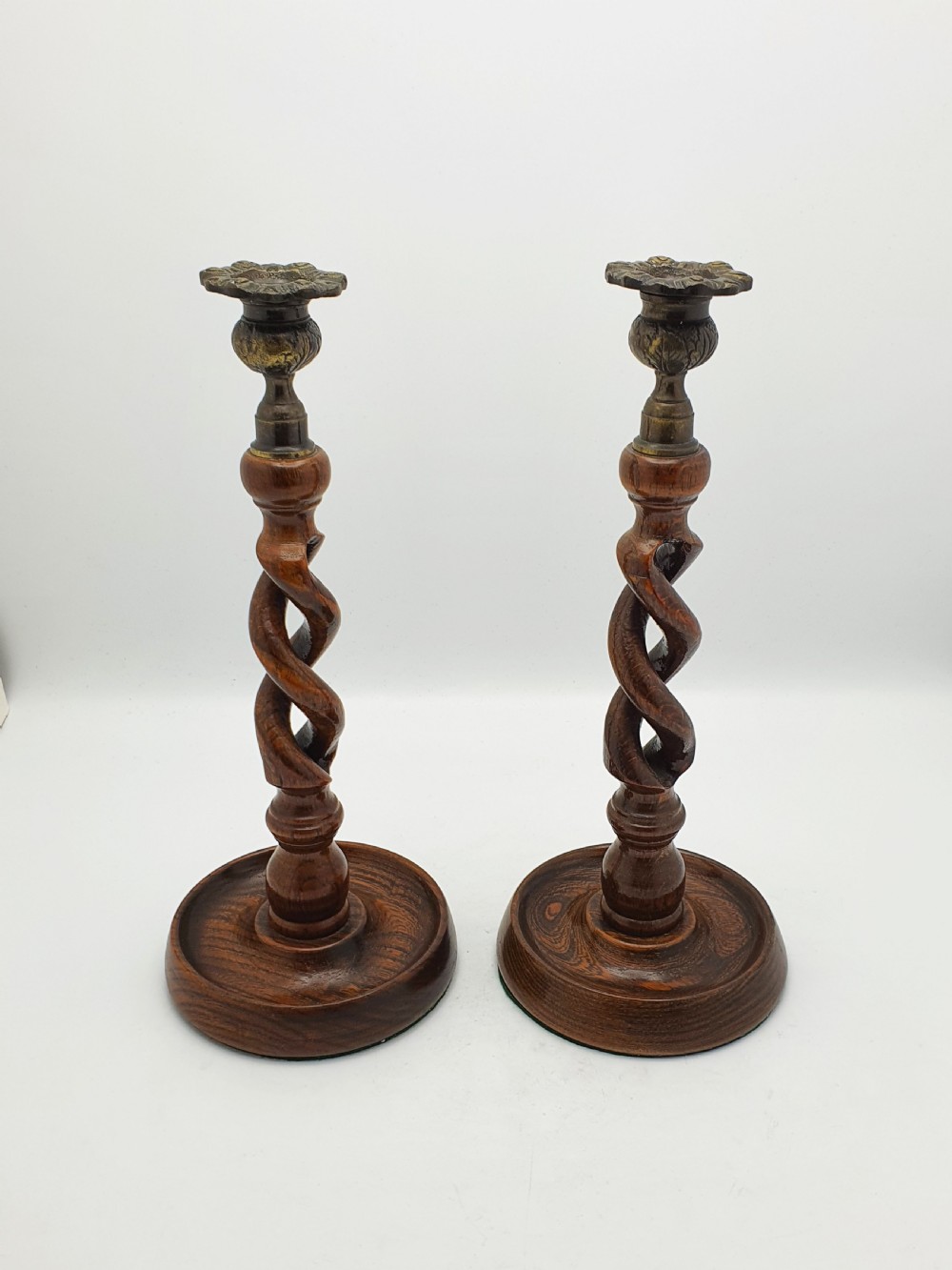 A pair of dark oak candlesticks featuring open barley twist stems and brass sconces atop round dished bases. View VIII