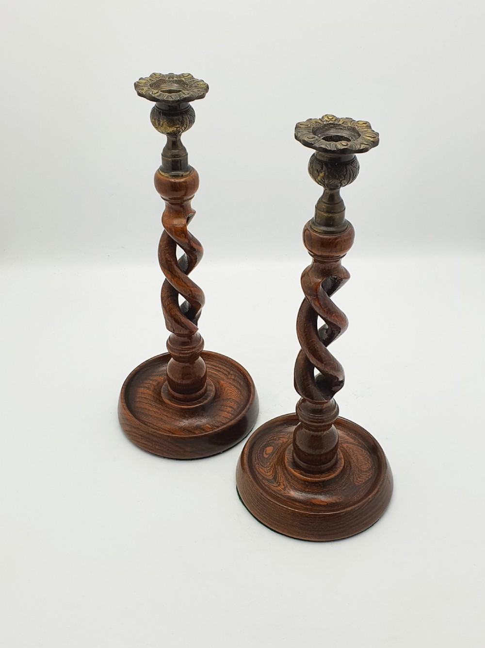 A pair of dark oak candlesticks featuring open barley twist stems and brass sconces atop round dished bases. View IX