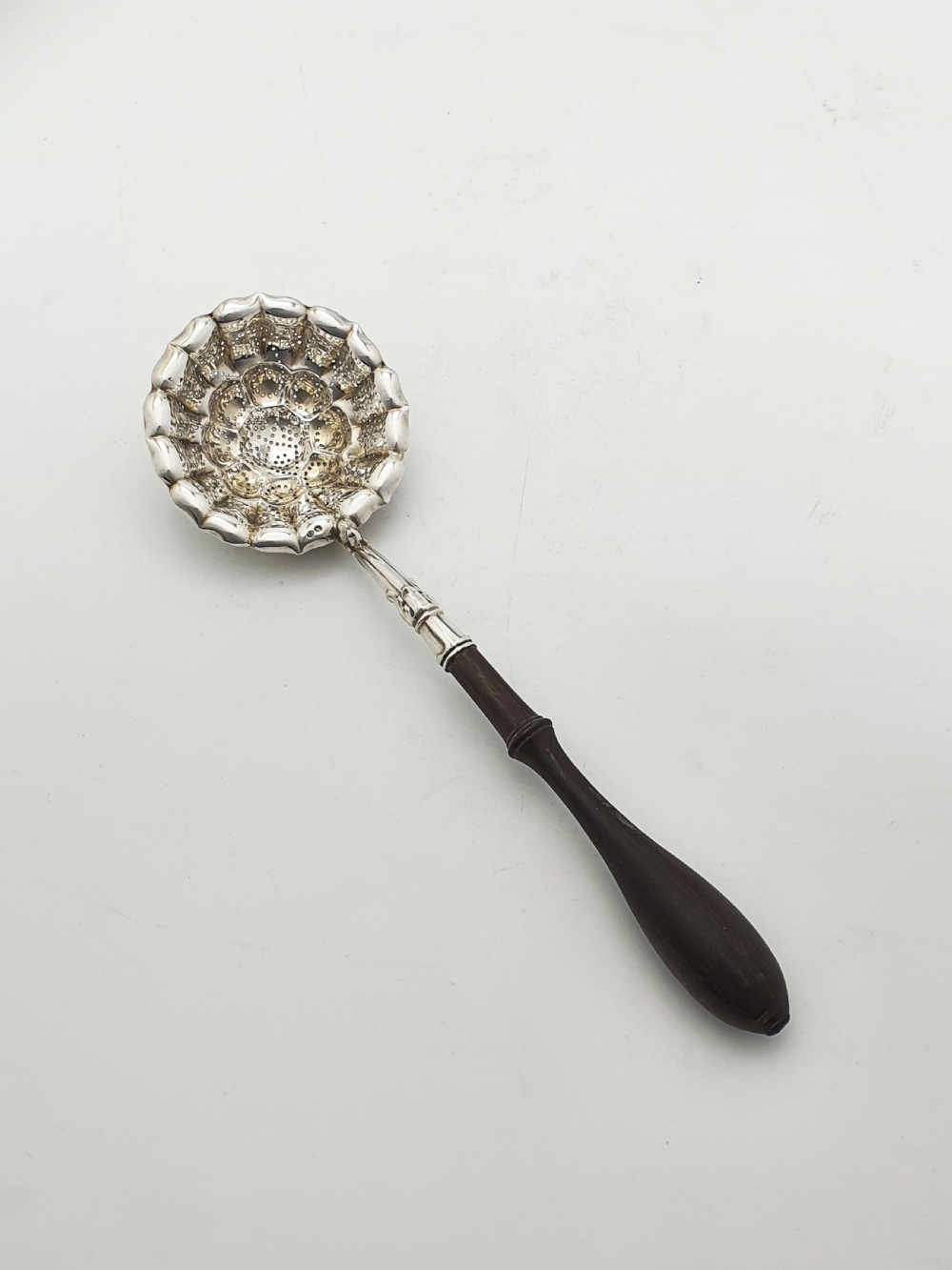 A late nineteenth-century Continental silver tea strainer featuring a fluted pierced bowl attached to a dark turned wooden handle.