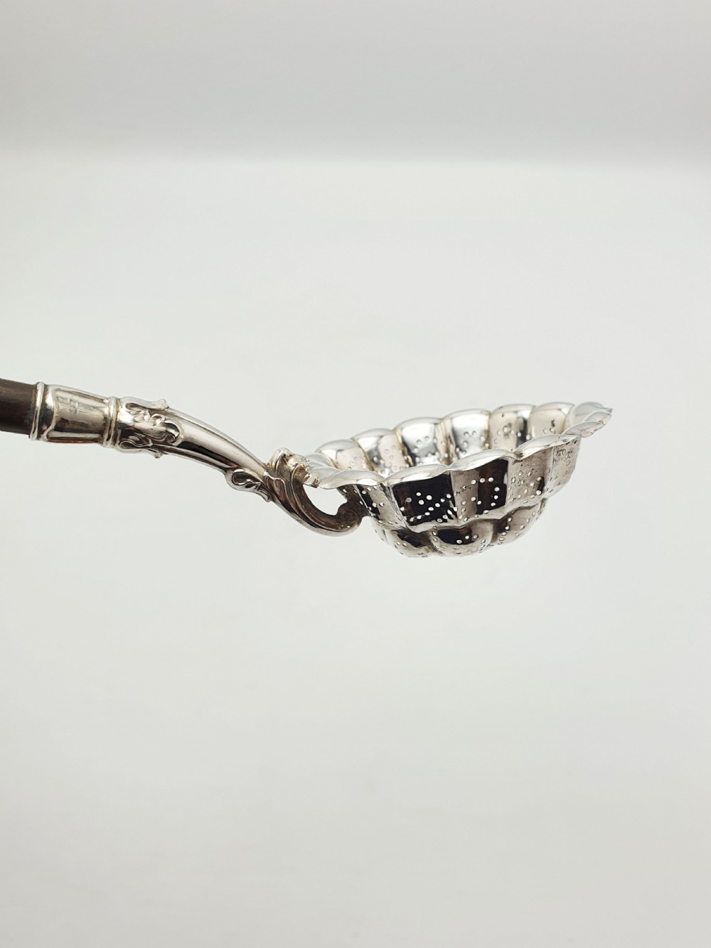 A late nineteenth-century Continental silver tea strainer featuring a fluted pierced bowl attached to a dark turned wooden handle. View VI