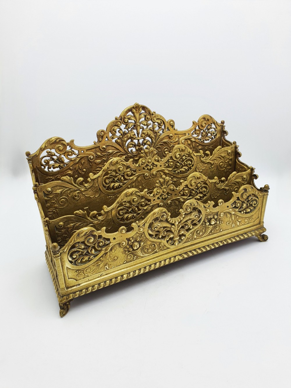 A cast brass Rococo Revival letter rack featuring three tiered compartments with intricate pierced scrollwork and foliate cresting.
