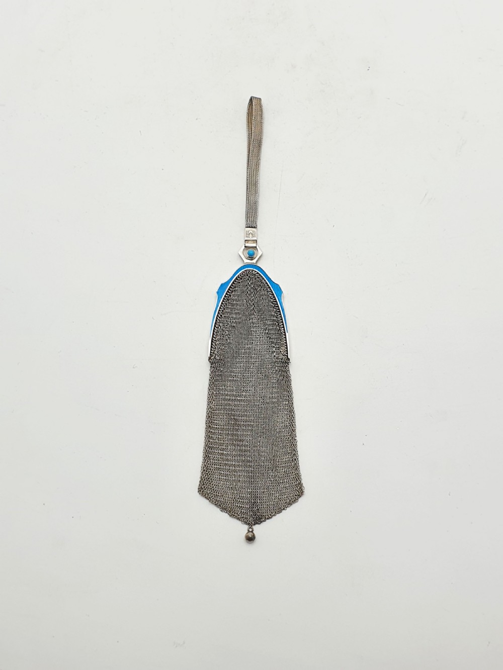 An antique silver mesh purse featuring a blue guilloche enamel top frame, a woven silver strap, and a hanging metal drop.