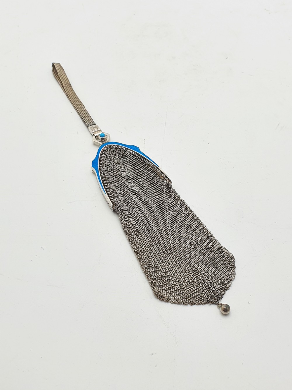 An antique silver mesh purse featuring a blue guilloche enamel top frame, a woven silver strap, and a hanging metal drop. View III
