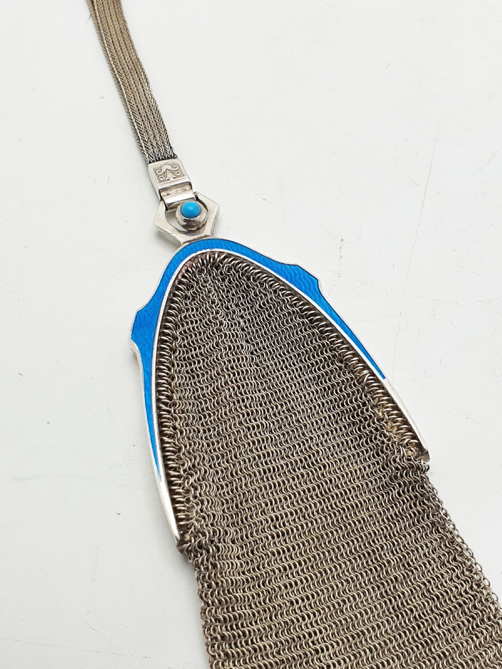 An antique silver mesh purse featuring a blue guilloche enamel top frame, a woven silver strap, and a hanging metal drop. View IV