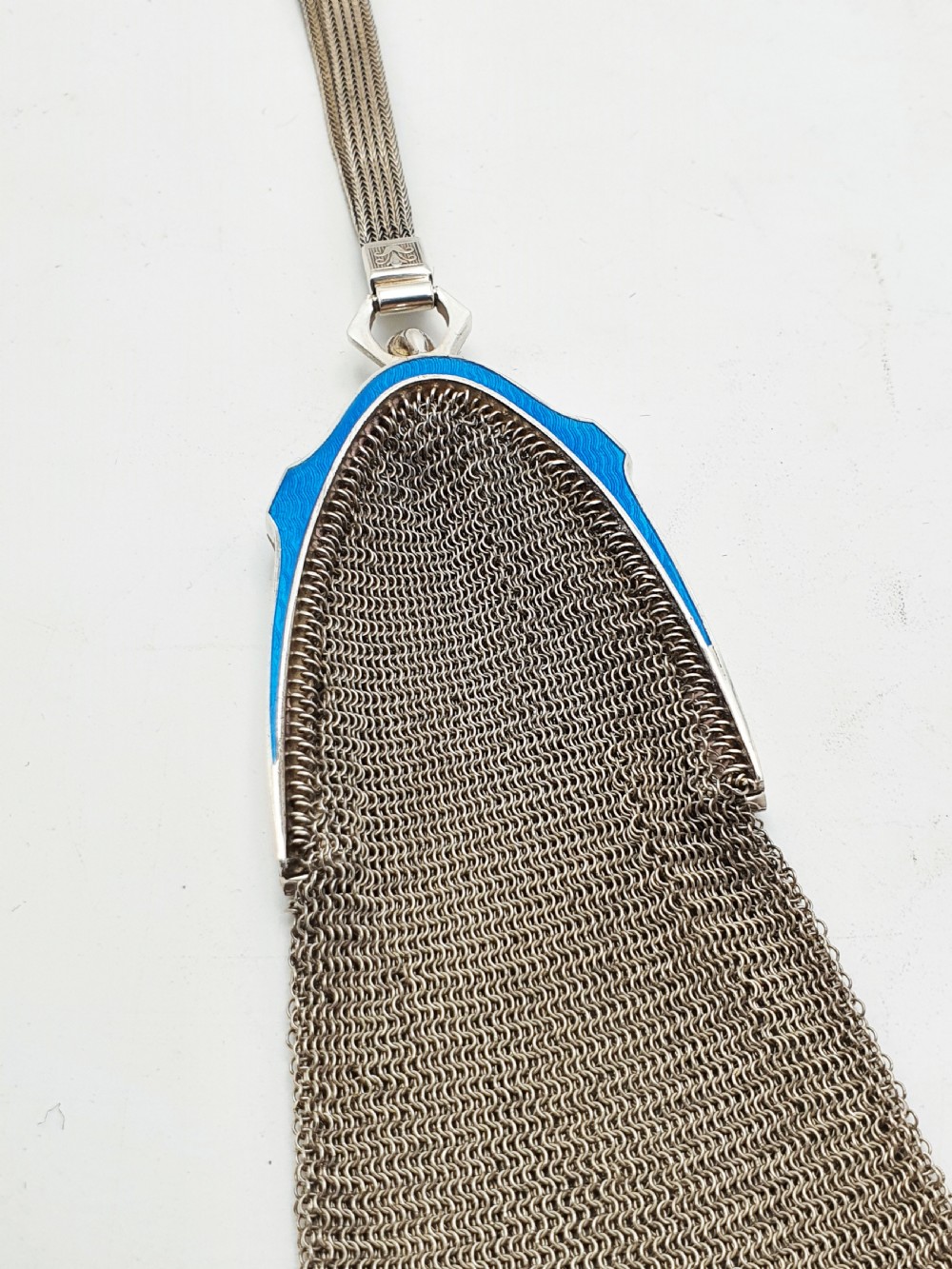 An antique silver mesh purse featuring a blue guilloche enamel top frame, a woven silver strap, and a hanging metal drop. View V