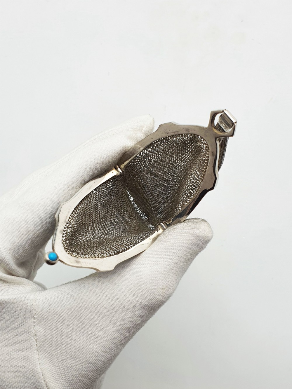 An antique silver mesh purse featuring a blue guilloche enamel top frame, a woven silver strap, and a hanging metal drop. View VI