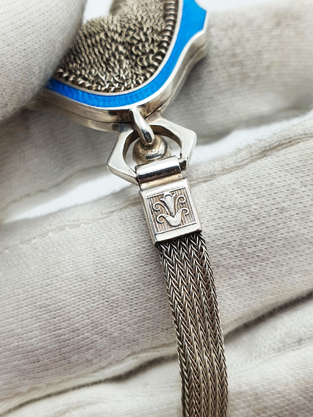 An antique silver mesh purse featuring a blue guilloche enamel top frame, a woven silver strap, and a hanging metal drop. View VIII