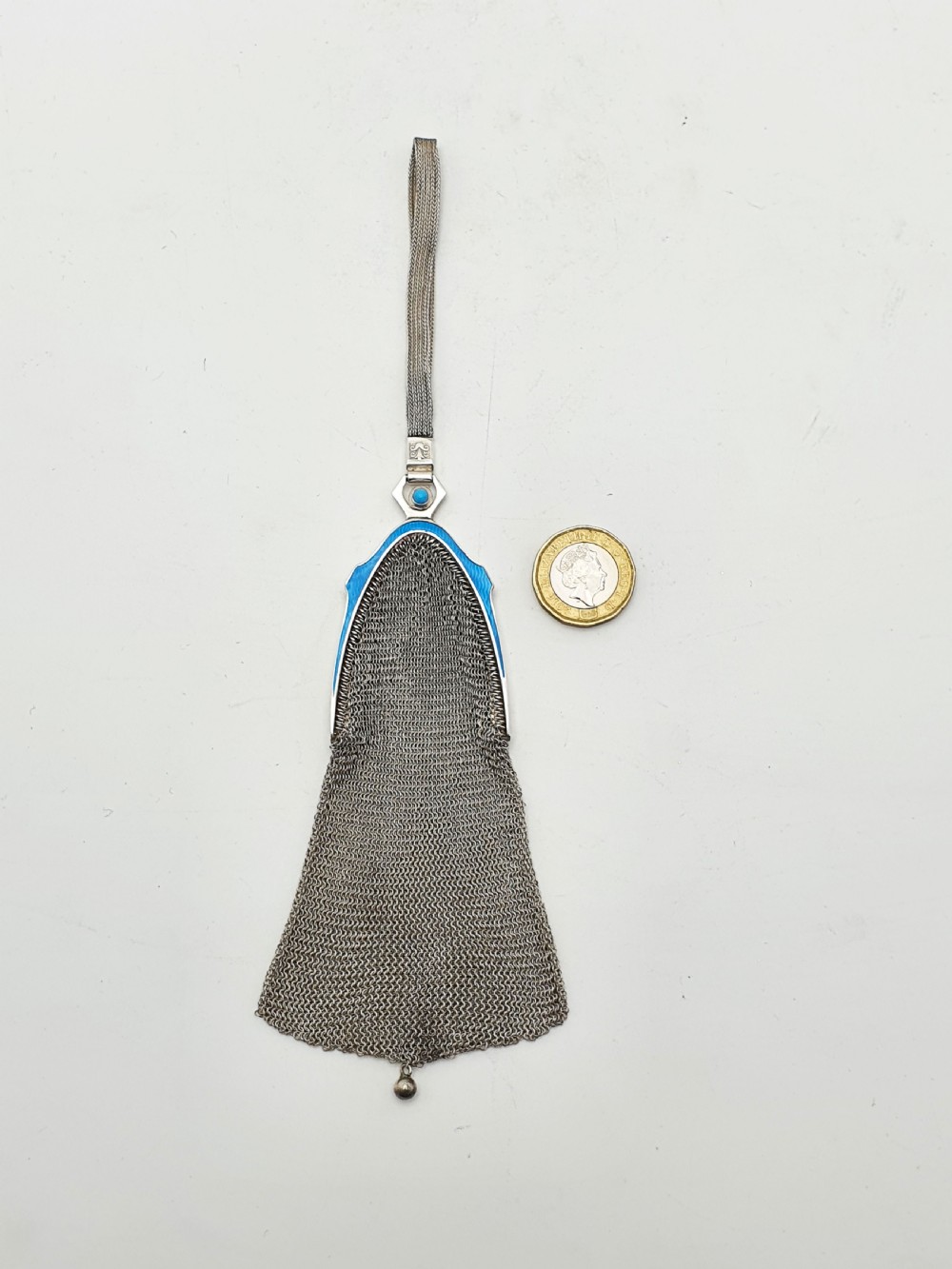 An antique silver mesh purse featuring a blue guilloche enamel top frame, a woven silver strap, and a hanging metal drop. View IX