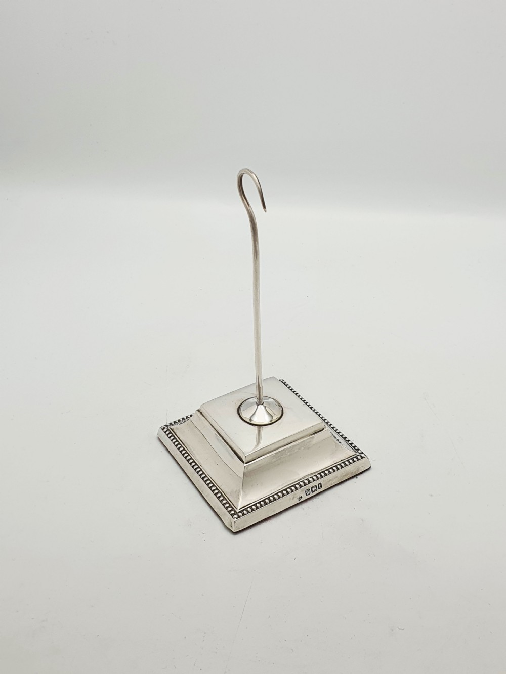 A late Victorian sterling silver receipt hook featuring a square stepped plinth base with beaded detail and a upright hooked stem.