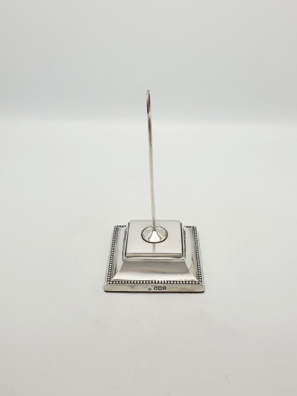 A late Victorian sterling silver receipt hook featuring a square stepped plinth base with beaded detail and a upright hooked stem. View II