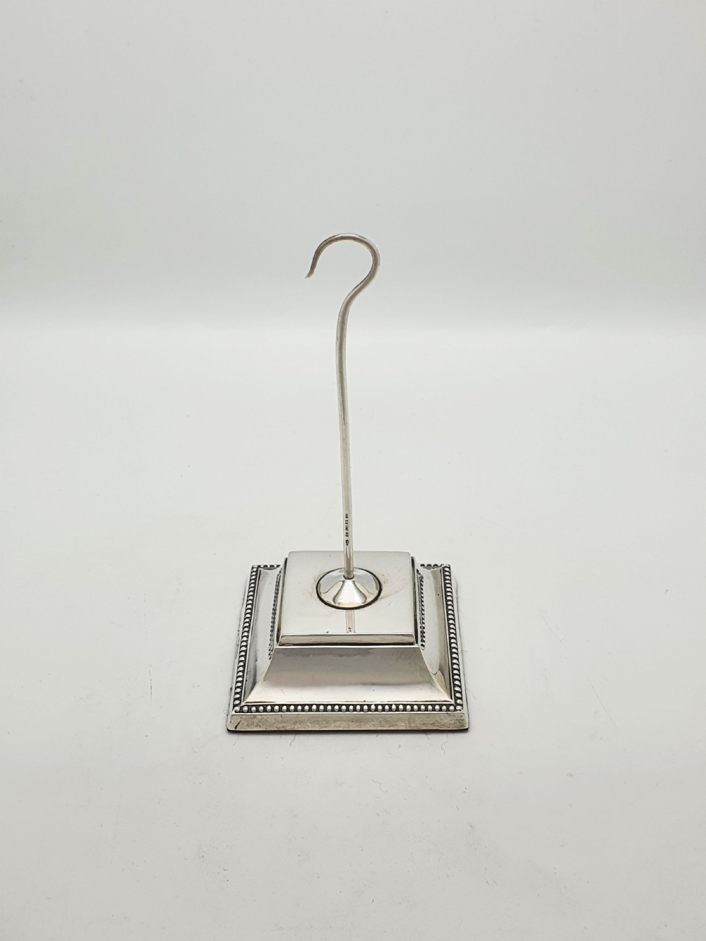 A late Victorian sterling silver receipt hook featuring a square stepped plinth base with beaded detail and a upright hooked stem. View III