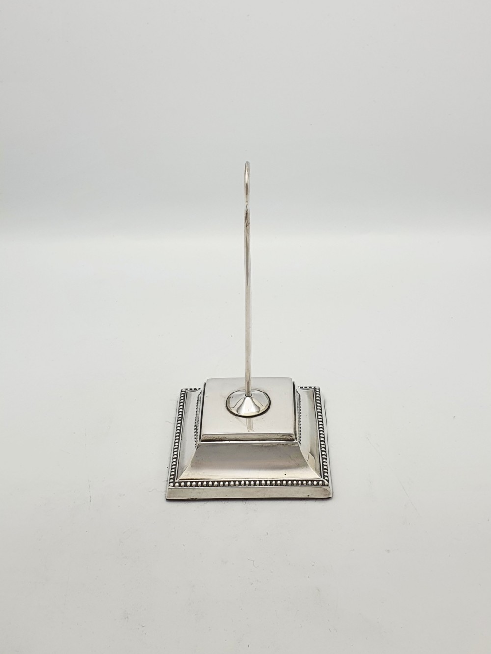 A late Victorian sterling silver receipt hook featuring a square stepped plinth base with beaded detail and a upright hooked stem. View IV