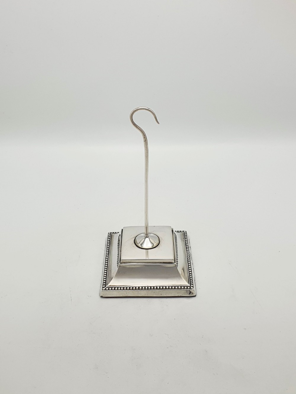 A late Victorian sterling silver receipt hook featuring a square stepped plinth base with beaded detail and a upright hooked stem. View V