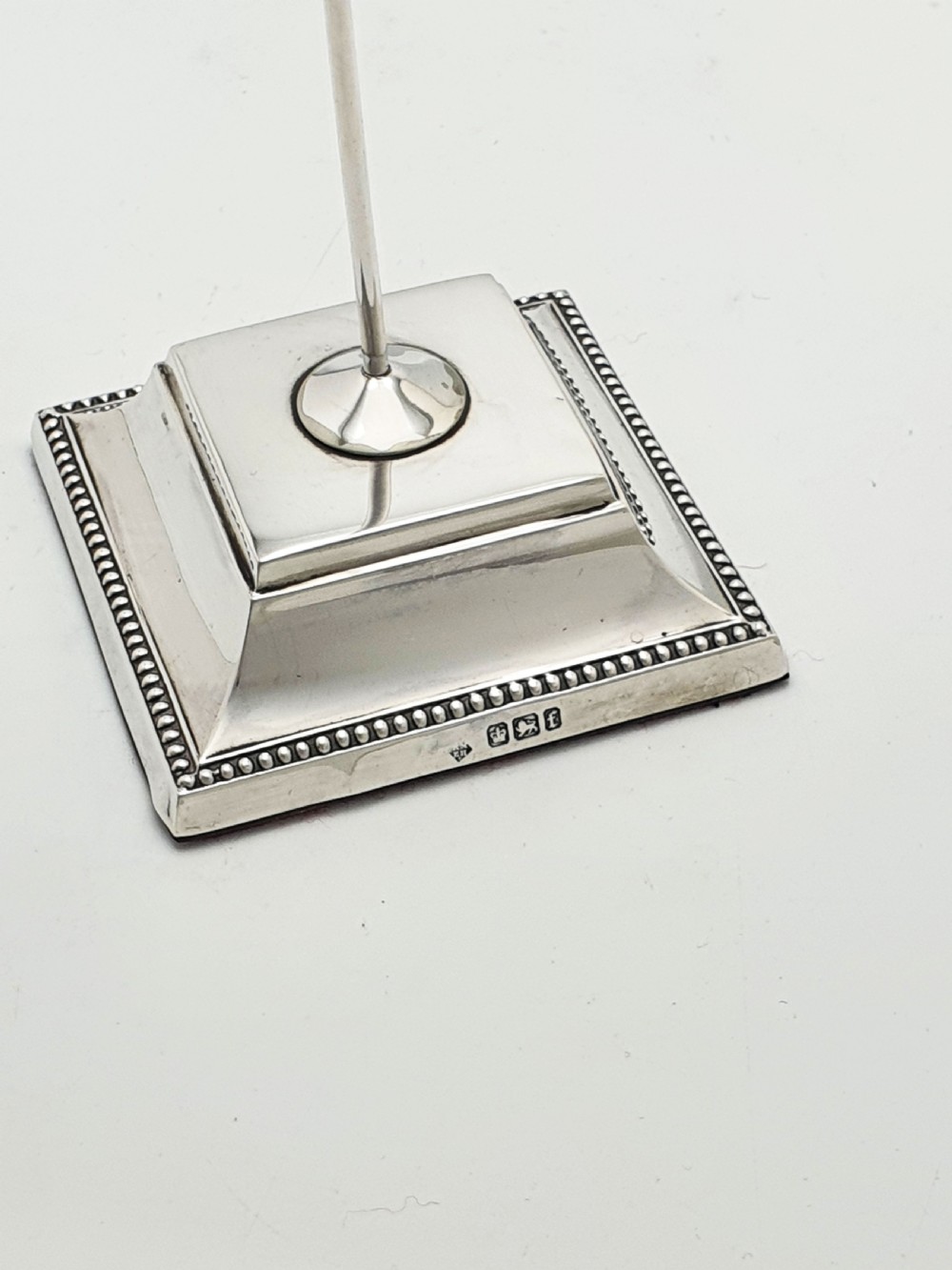A late Victorian sterling silver receipt hook featuring a square stepped plinth base with beaded detail and a upright hooked stem. View VI