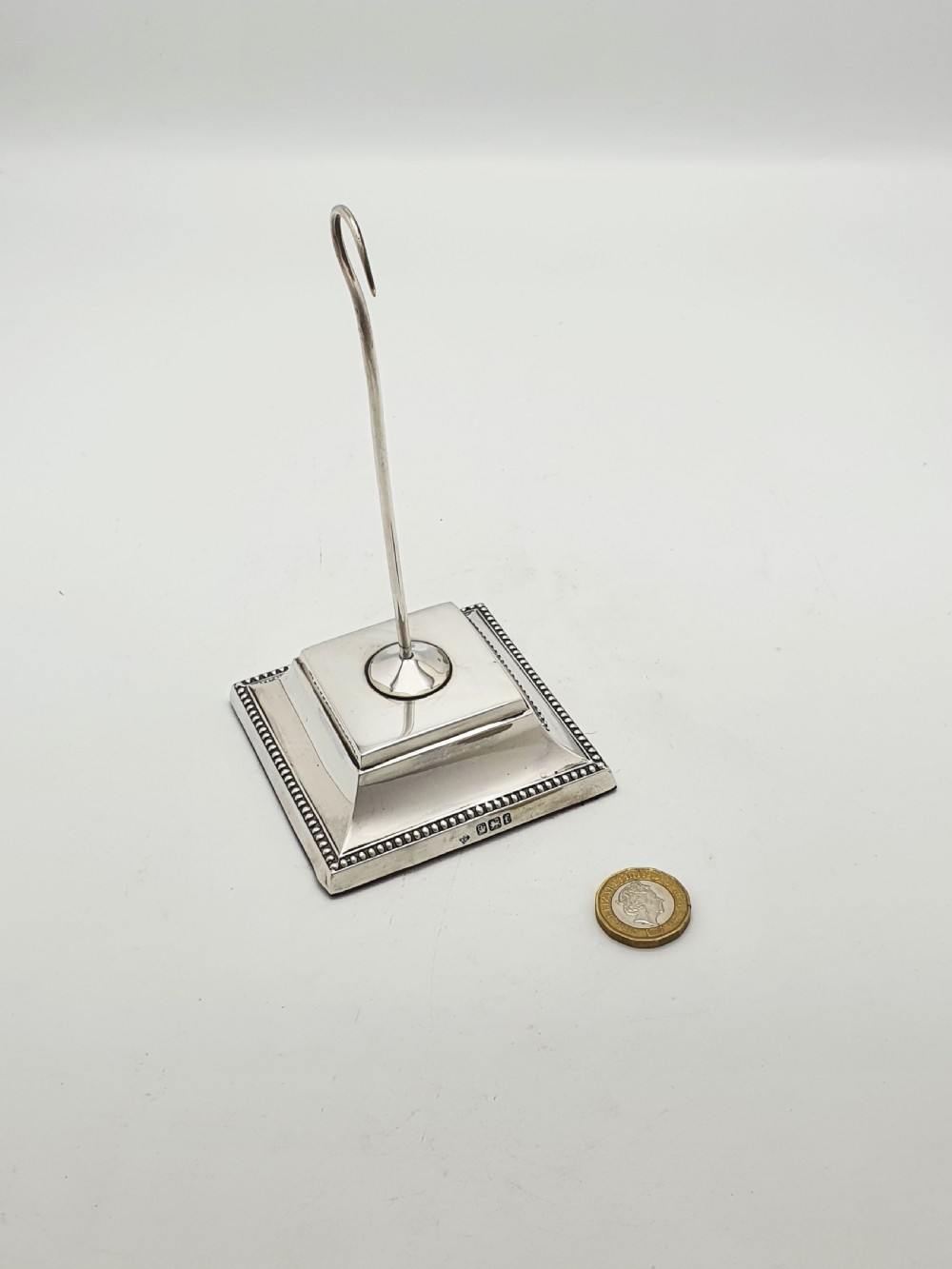 A late Victorian sterling silver receipt hook featuring a square stepped plinth base with beaded detail and a upright hooked stem. View X