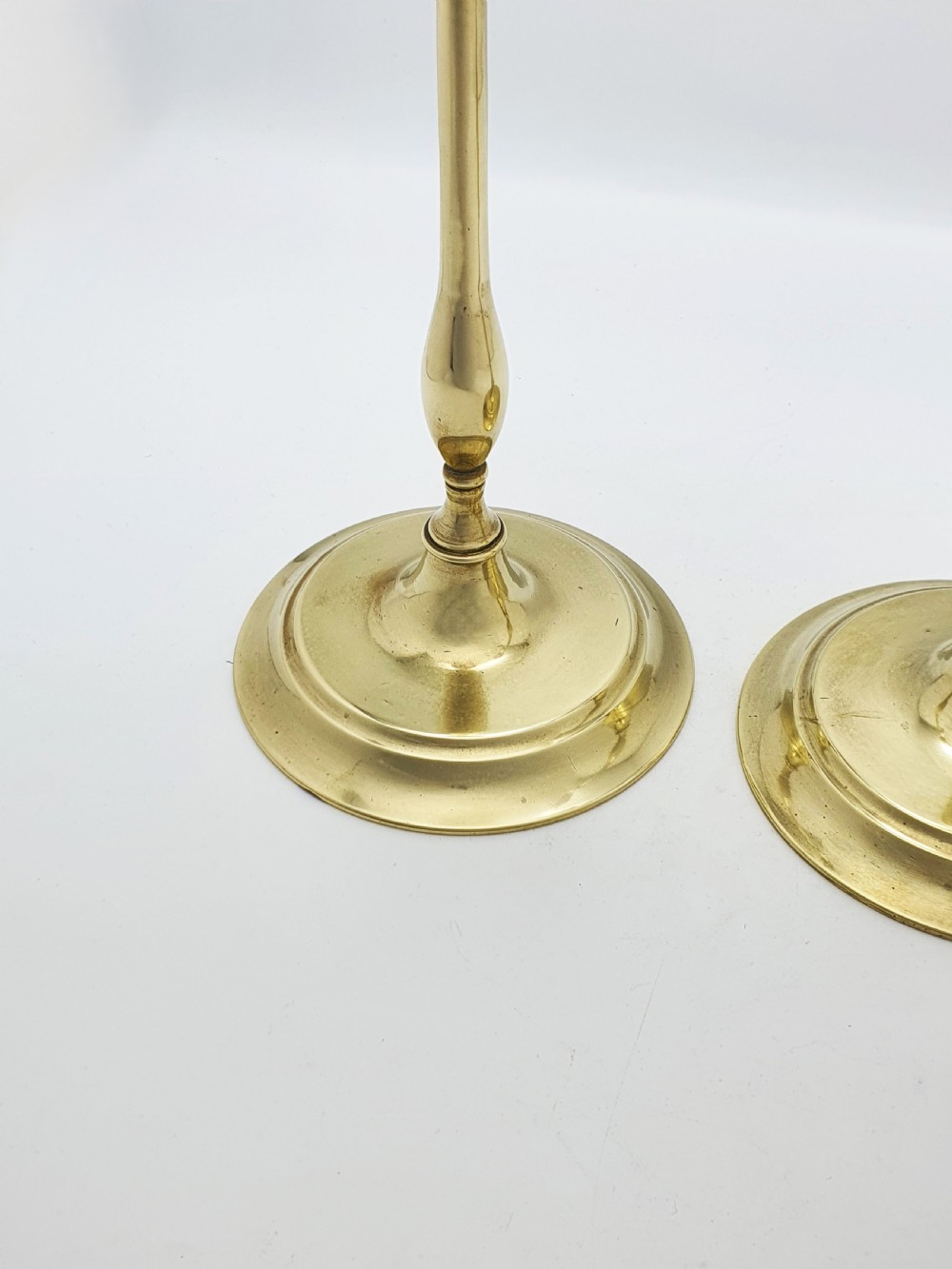 A pair of tall antique Edwardian brass candlesticks featuring slender turned stems, wide drip pans, and circular stepped bases. View III