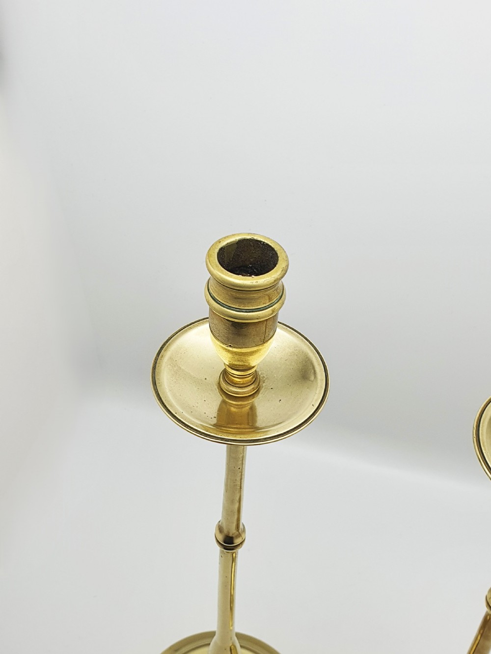 A pair of tall antique Edwardian brass candlesticks featuring slender turned stems, wide drip pans, and circular stepped bases. View IV