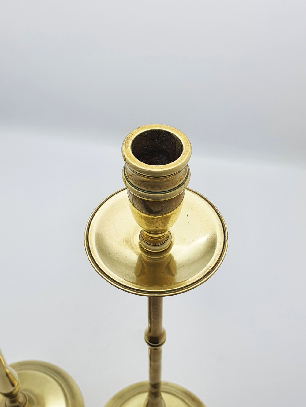 A pair of tall antique Edwardian brass candlesticks featuring slender turned stems, wide drip pans, and circular stepped bases. View V