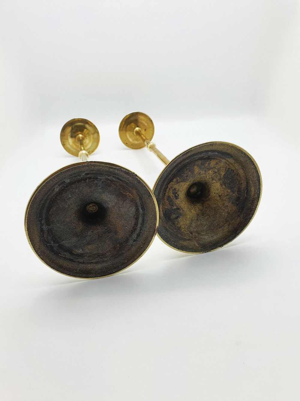 A pair of tall antique Edwardian brass candlesticks featuring slender turned stems, wide drip pans, and circular stepped bases. View VI