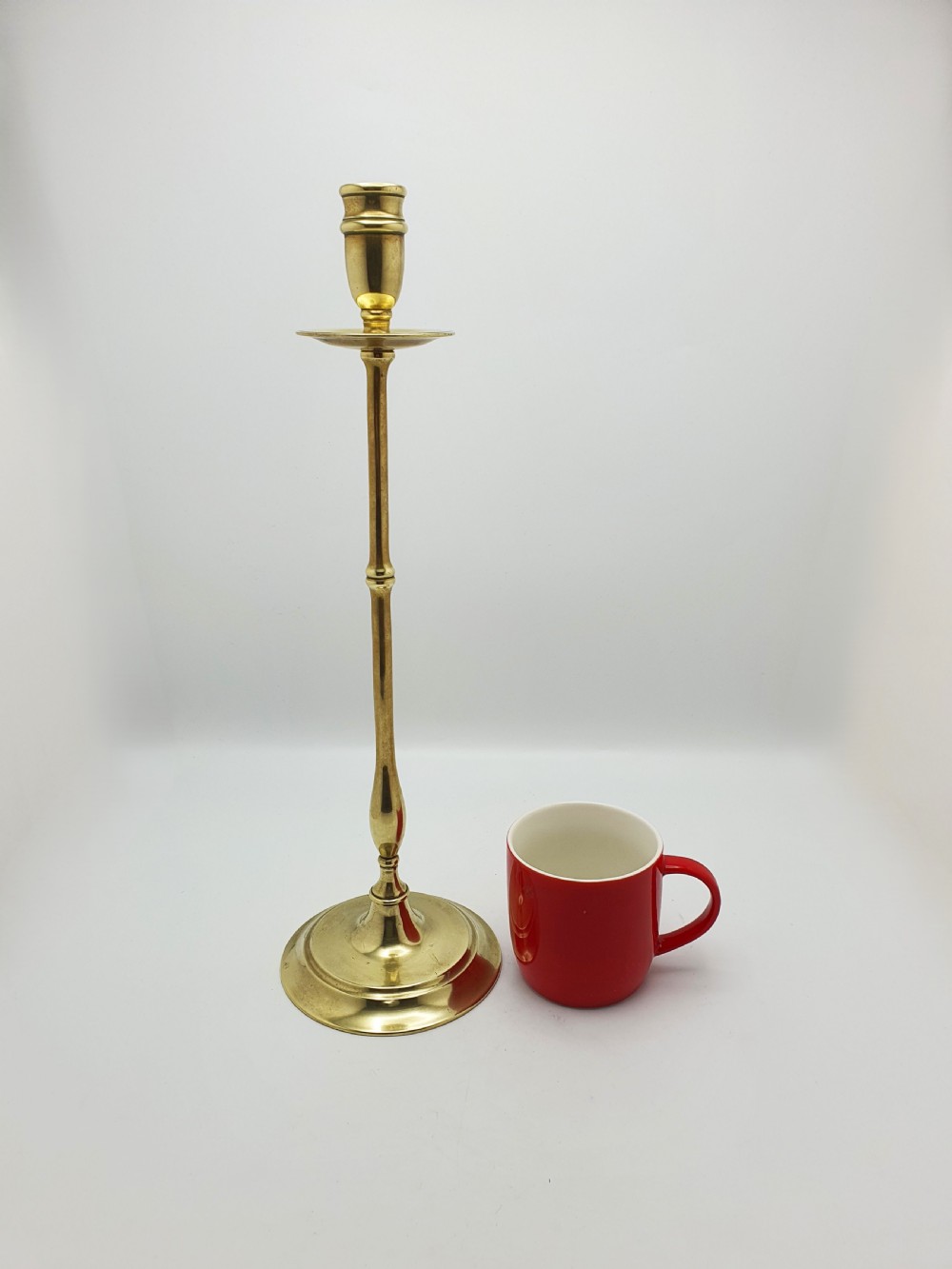 A pair of tall antique Edwardian brass candlesticks featuring slender turned stems, wide drip pans, and circular stepped bases. View VII