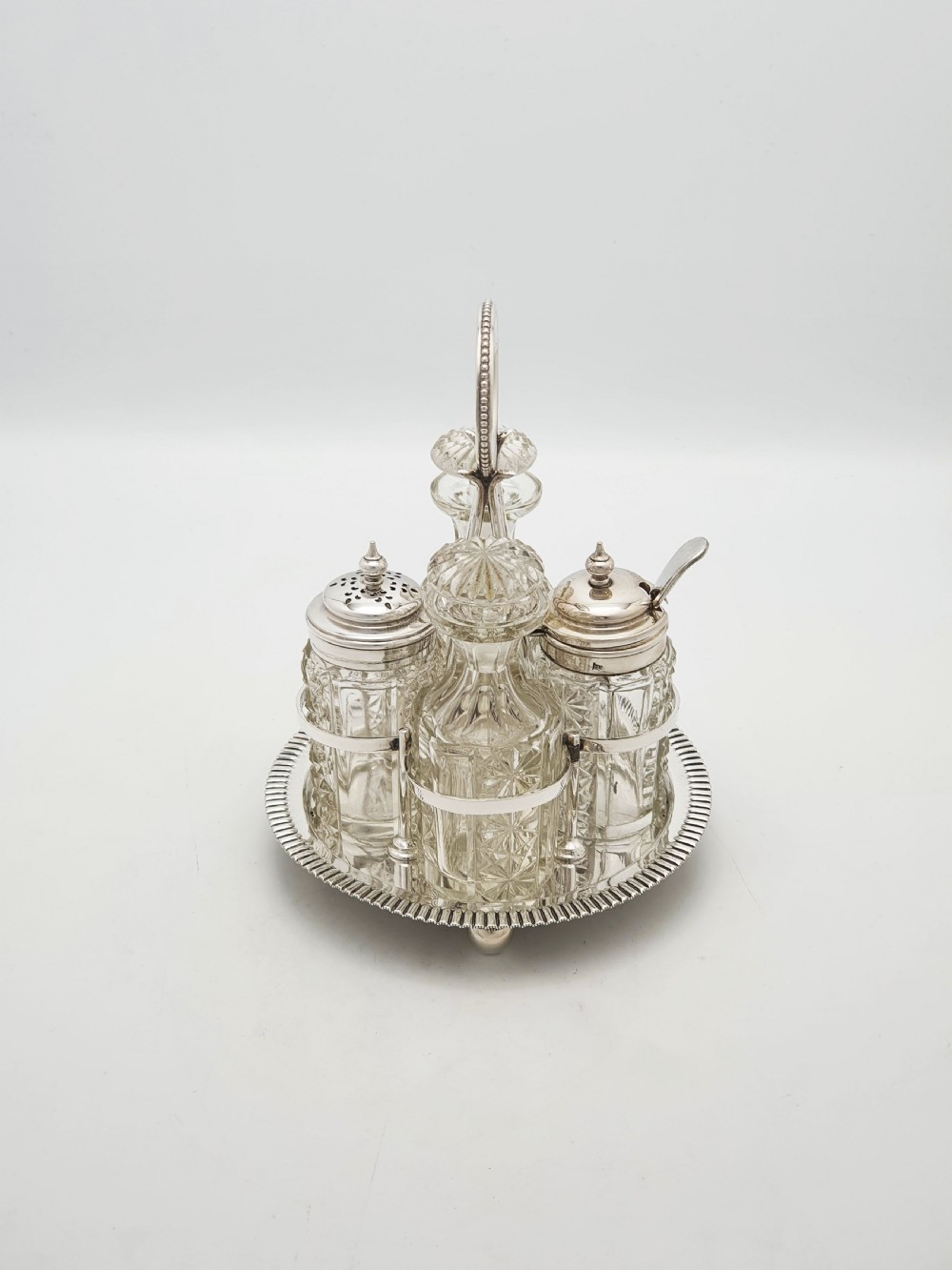An antique silver-plated bachelor cruet set featuring cut-glass bottles on a circular gadrooned tray with a central carrying handle. View III