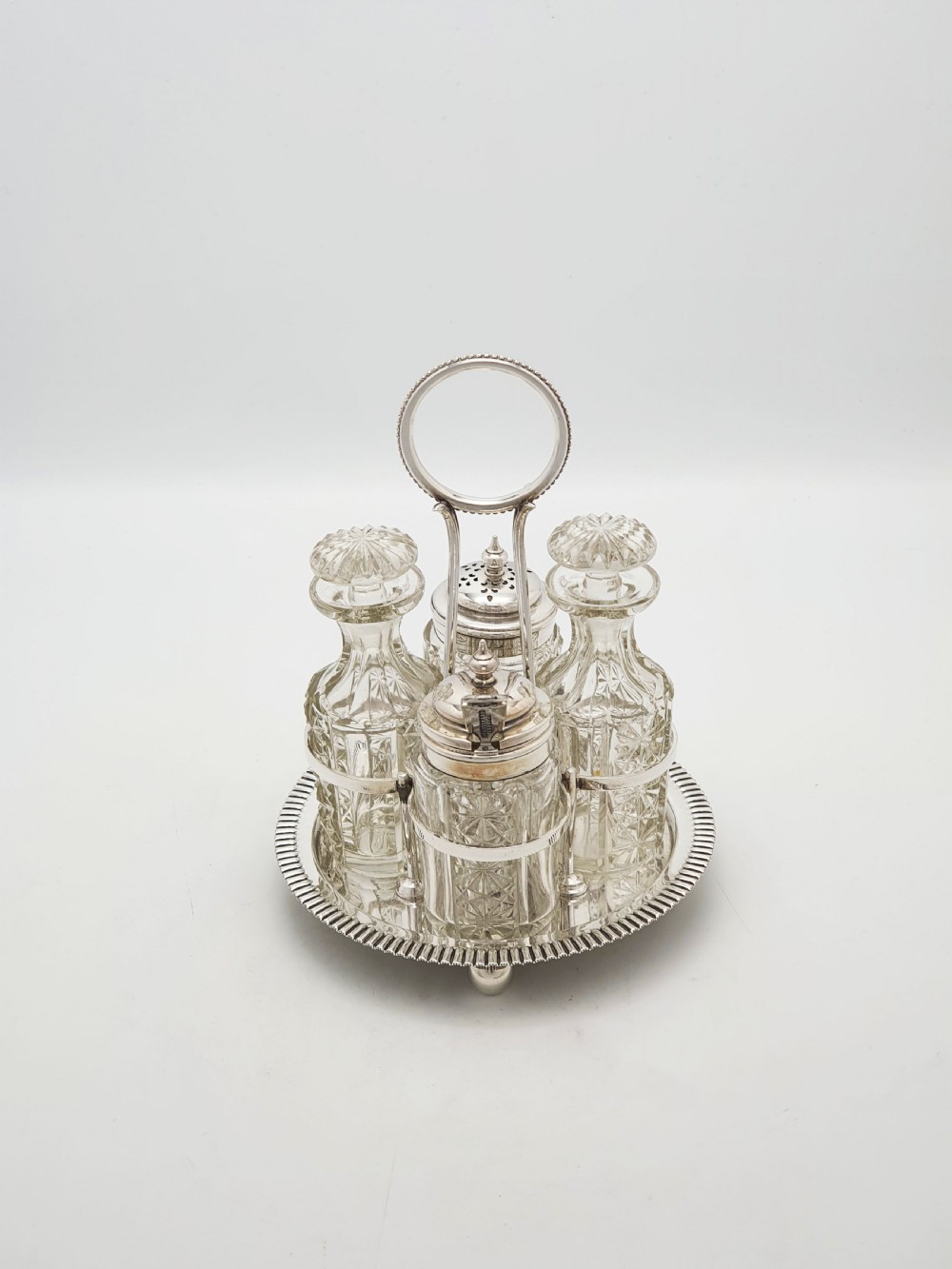 An antique silver-plated bachelor cruet set featuring cut-glass bottles on a circular gadrooned tray with a central carrying handle. View IV