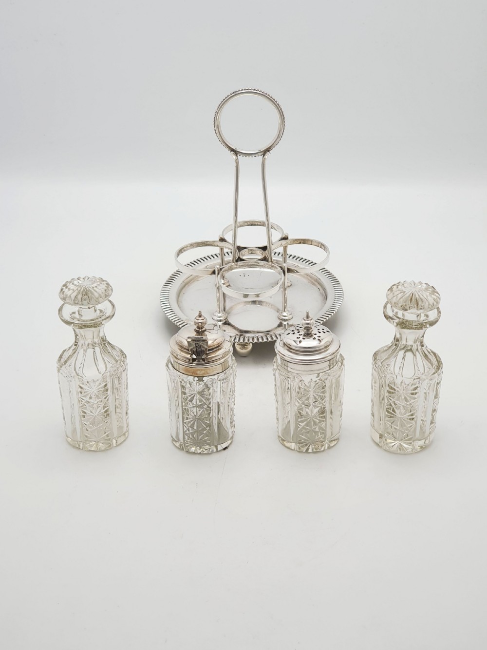 An antique silver-plated bachelor cruet set featuring cut-glass bottles on a circular gadrooned tray with a central carrying handle. View VI