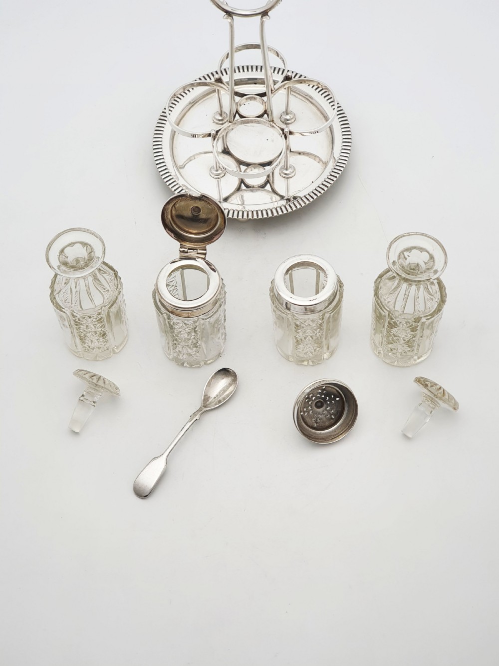 An antique silver-plated bachelor cruet set featuring cut-glass bottles on a circular gadrooned tray with a central carrying handle. View VII