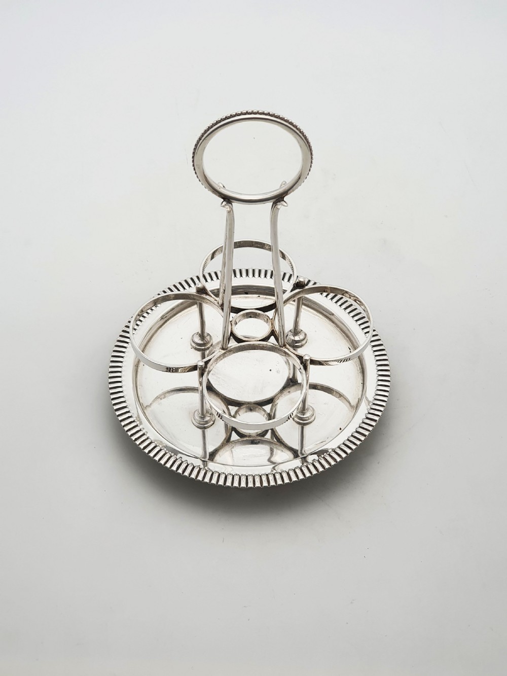 An antique silver-plated bachelor cruet set featuring cut-glass bottles on a circular gadrooned tray with a central carrying handle. View VIII