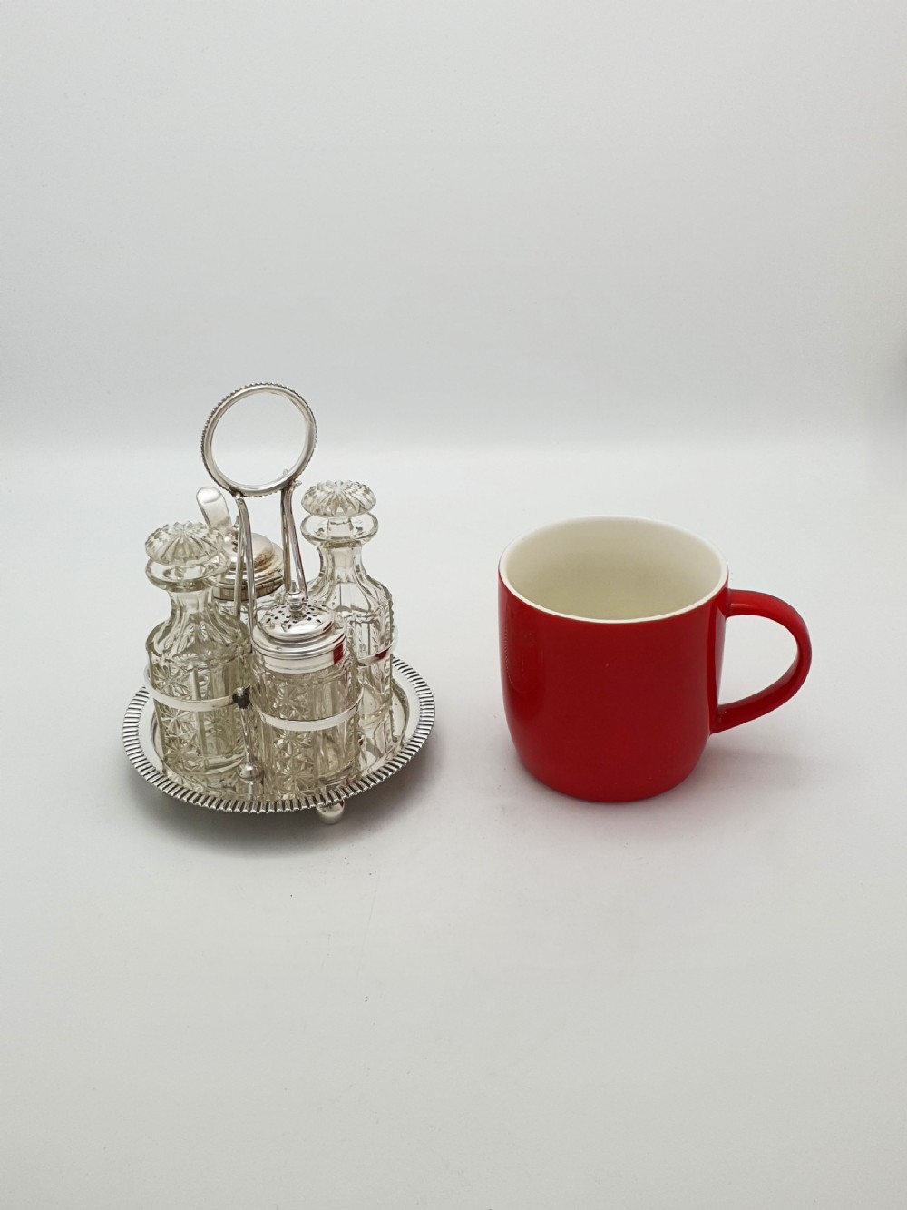 An antique silver-plated bachelor cruet set featuring cut-glass bottles on a circular gadrooned tray with a central carrying handle. View X