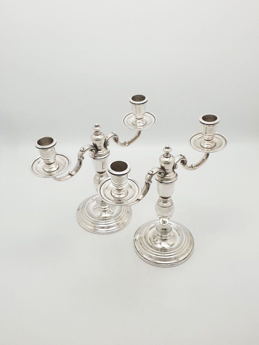 A pair of silver-plated low two-branch candelabra featuring turned central stems, circular stepped bases, and scrolled arms.