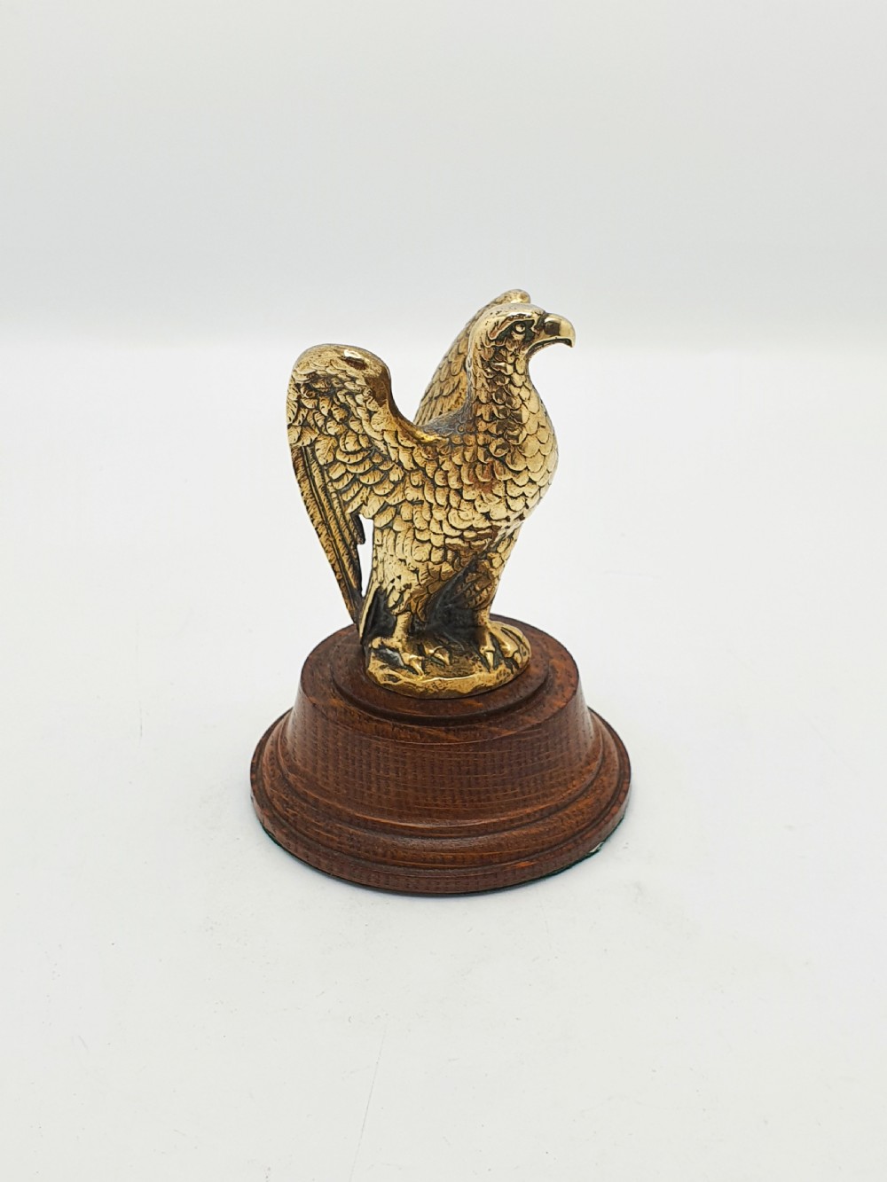 A cast brass eagle figurine with detailed feather engraving, mounted on a stepped circular dark wooden base.