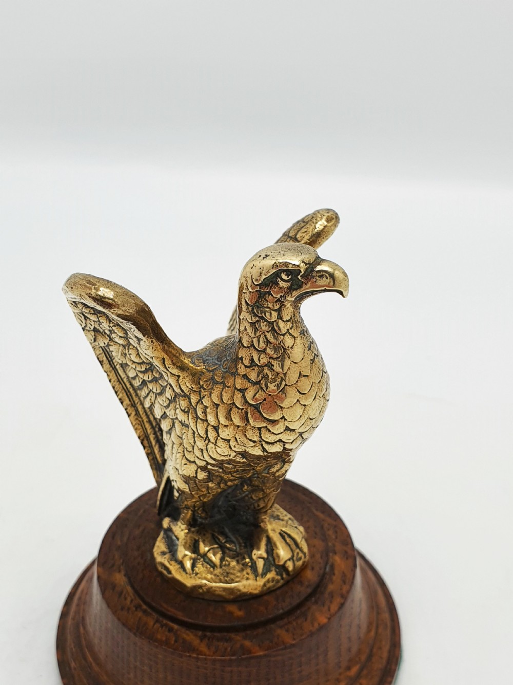 A cast brass eagle figurine with detailed feather engraving, mounted on a stepped circular dark wooden base. View II