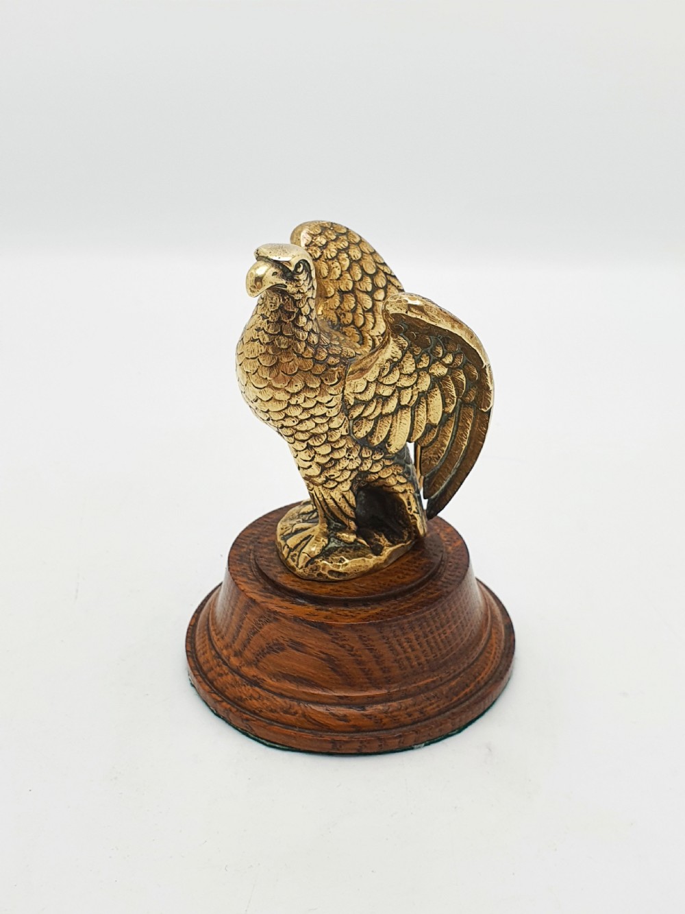 A cast brass eagle figurine with detailed feather engraving, mounted on a stepped circular dark wooden base. View III