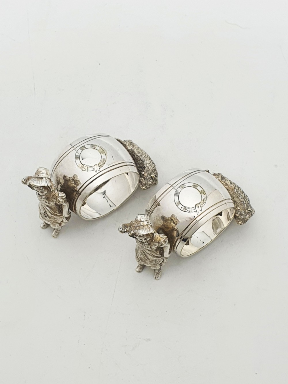 A pair of Victorian silver-plated napkin rings featuring detailed cast figures of young girls wearing bonnets standing beside engraved circular rings. View II