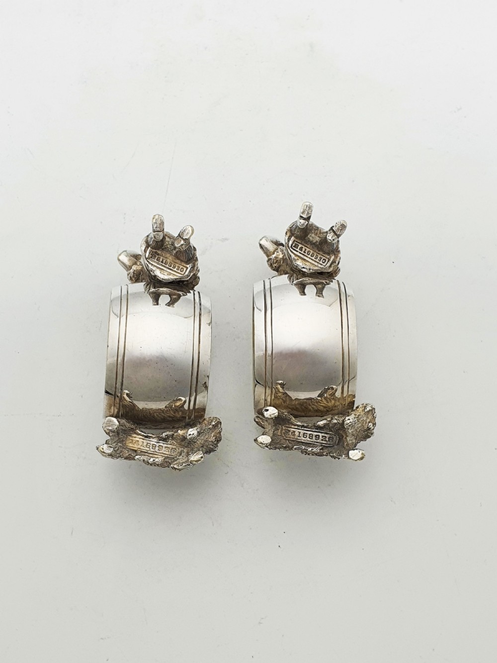 A pair of Victorian silver-plated napkin rings featuring detailed cast figures of young girls wearing bonnets standing beside engraved circular rings. View VI