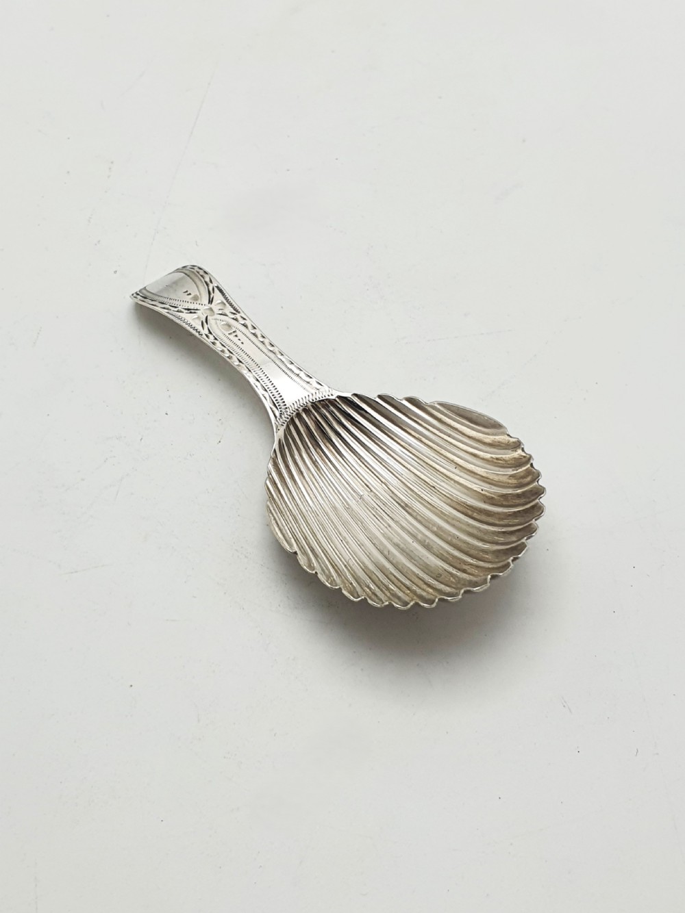 A Georgian sterling silver caddy spoon featuring a fluted shell bowl and an engraved bright-cut handle.