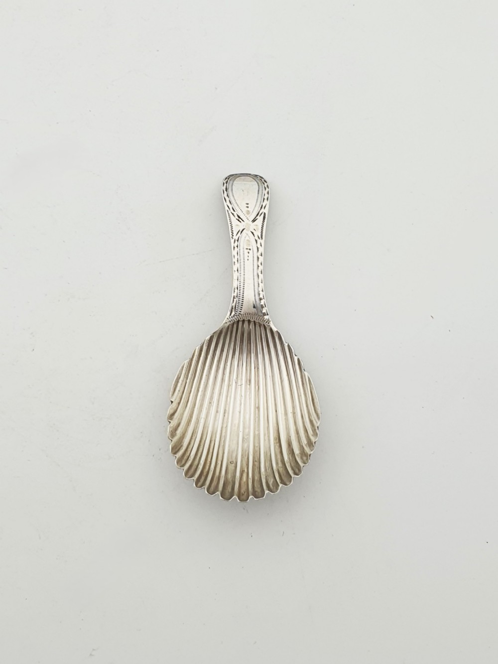 A Georgian sterling silver caddy spoon featuring a fluted shell bowl and an engraved bright-cut handle. View II
