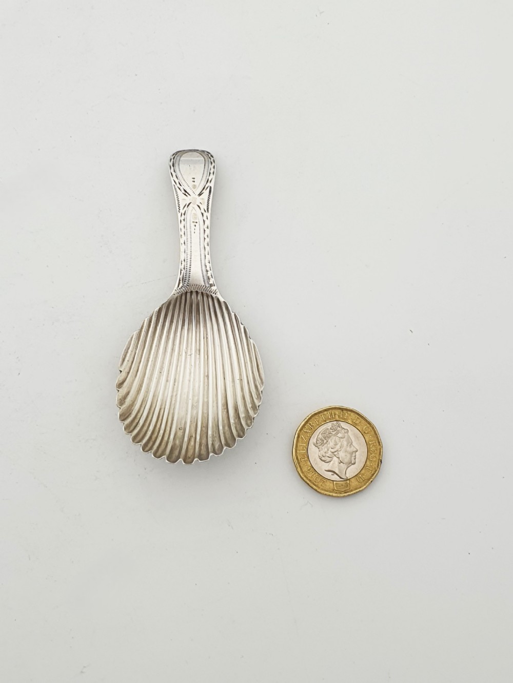 A Georgian sterling silver caddy spoon featuring a fluted shell bowl and an engraved bright-cut handle. View V