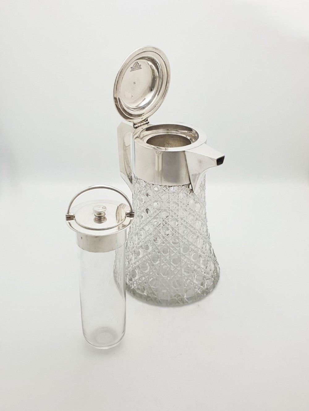 An antique Victorian cut glass lemonade jug featuring a silver-plated hinged lid and spout alongside its removable clear glass ice tube insert.
