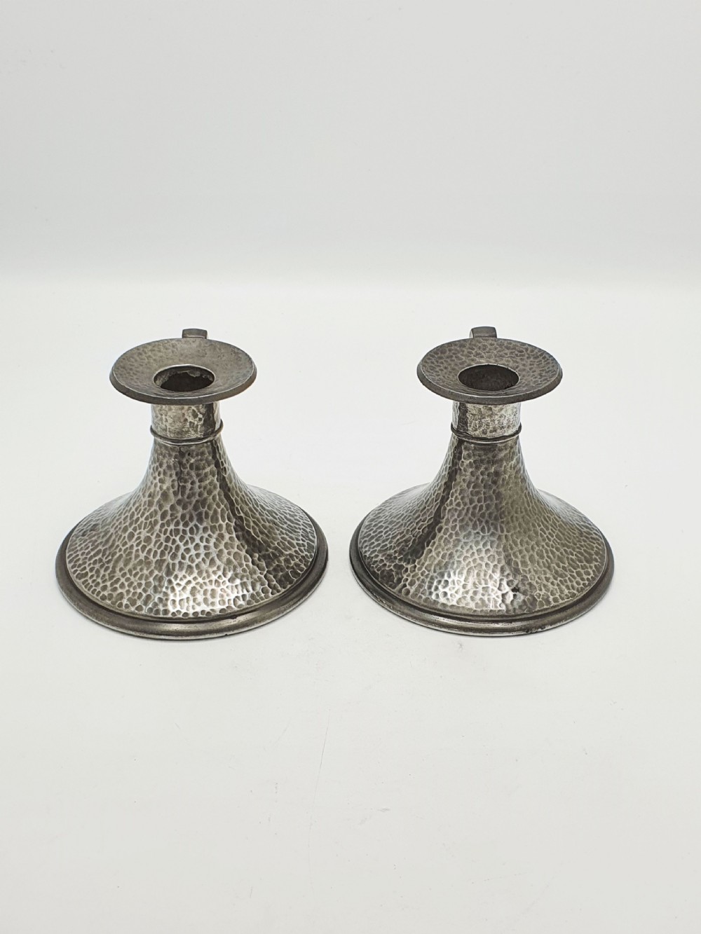A pair of Arts and Crafts era flared pewter chambersticks with hand-hammered textures and curved side handles. View III