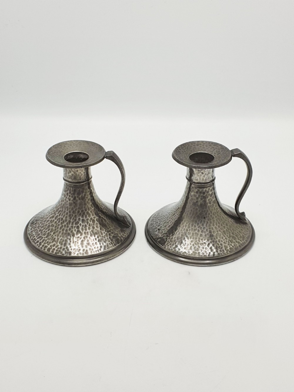A pair of Arts and Crafts era flared pewter chambersticks with hand-hammered textures and curved side handles. View IV