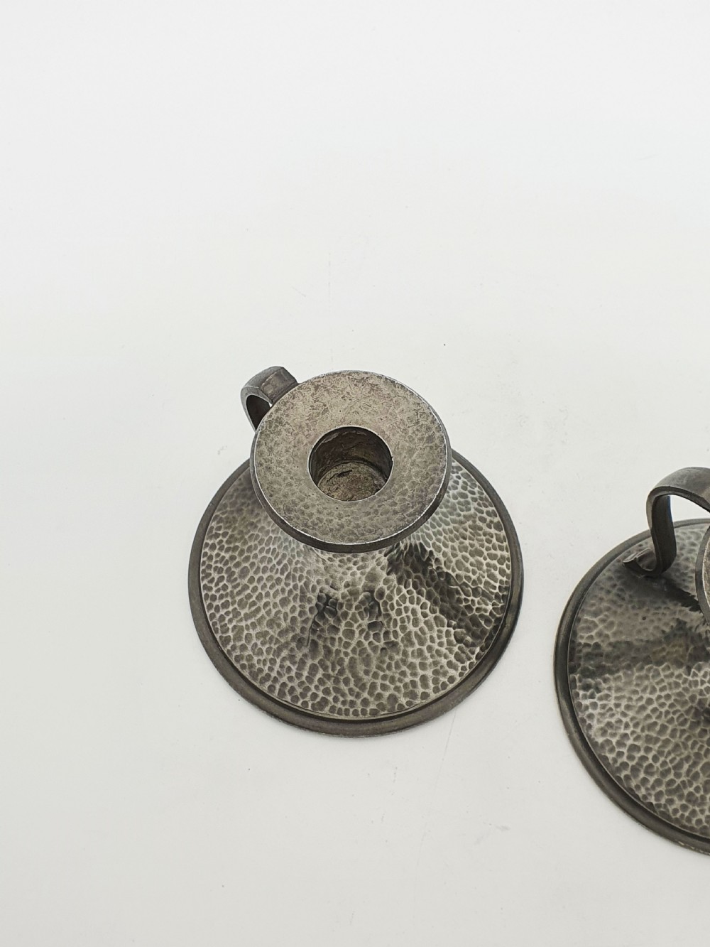 A pair of Arts and Crafts era flared pewter chambersticks with hand-hammered textures and curved side handles. View VI