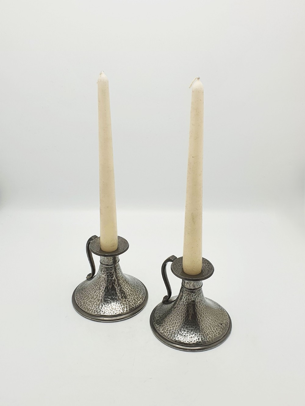A pair of Arts and Crafts era flared pewter chambersticks with hand-hammered textures and curved side handles. View VIII