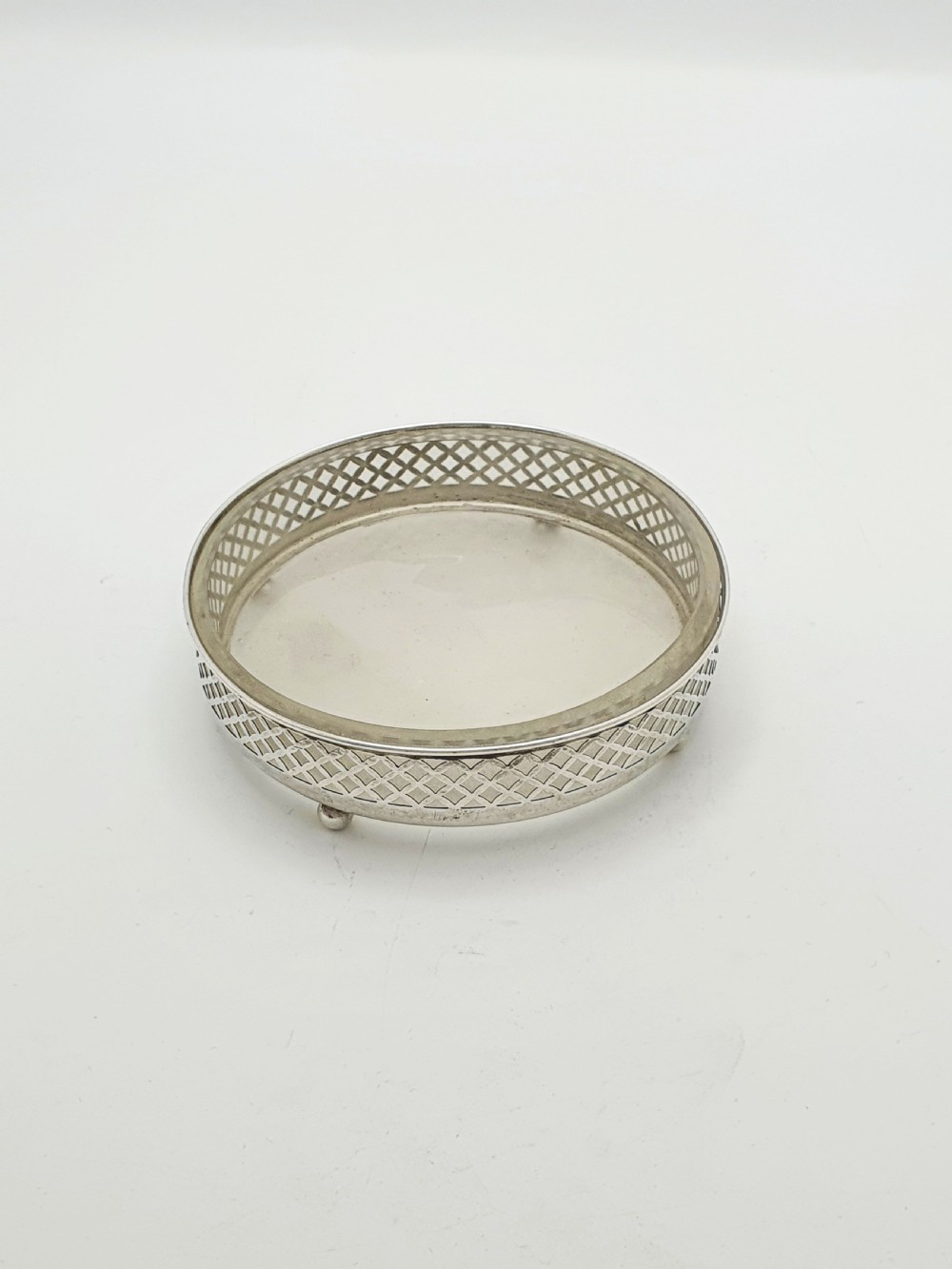A circular sterling silver dish with a pierced lattice pattern, raised on small ball feet, fitted with a clear glass insert.